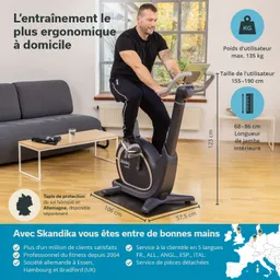 Heimtrainer im Wohnzimmer, Person sitzt darauf. Im Hintergrund Sofa und Tisch, Informationen zu Produktmerkmalen.