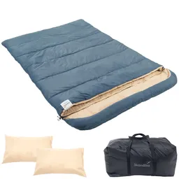 Blaue Schlafsack-Decke mit beiger Innenseite, zwei helle Kissen und schwarzer Tragetasche.