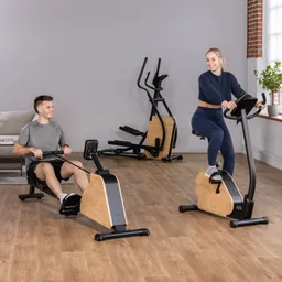 Zwei Personen trainieren in einem modernen Fitnessraum. Eine Person sitzt an einem Rudergerät, die andere fährt auf einem Heimtrainer. Beide Geräte haben Holz- und Metallverarbeitung. Im Hintergrund sind eine Couch und weitere Fitnessgeräte sichtbar.