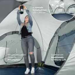 Eine Person steht im Inneren eines Zeltes und hält eine Lampe über den Kopf. Das Zelt hat drei separate Schlafkabinen.