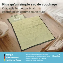 Grüner Schlafsack mit Drachenmotiv, auf einem Holzfußboden ausgebreitet. Links steht ein kleiner Tisch. Text in französischer Sprache.