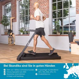 Mann joggt auf einem schwarzen Laufband in einem hellen Raum mit großen Fenstern. Pflanzen und Fitnessgeräte im Hintergrund.