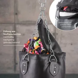 Schwarze Tasche mit Metallkette und Reißverschluss, gefüllt mit bunten Stoffabschnitten. Hintergrund ist grau.