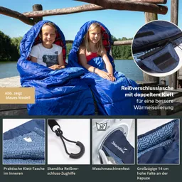 Zwei Kinder sitzen auf einer Holzplattform am Wasser in blauen Schlafsäcken.