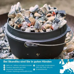 Schwarzer Topf mit glühenden Kohlen, die oben sichtbar sind. Hintergrund unscharf, mit einem grauen Boden.