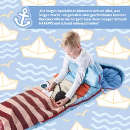 Ein Kind sitzt in einem bunten Schlafsack mit einem Motiv. Es hält ein Blatt Papier in der Hand. Der Hintergrund zeigt ein maritimes Muster mit Booten und Wellen.