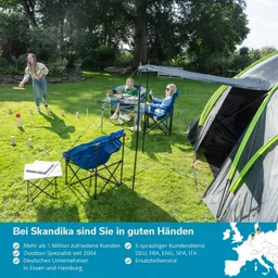 Drei Personen im Freien, auf einem grünen Rasen. Eine Person wirft einen Gegenstand, zwei sitzen an einem Tisch. Ein Zelt im Hintergrund.