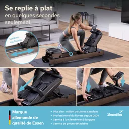 Fitnessgerät zum Rudern mit einer Person, die es handhabt. Holzrahmen, zusammenklappbar, auf einem Teppich in modernem Raum.