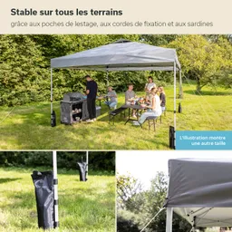 Ein graues, faltbares Blattdach steht auf einem Rasen, umgeben von Bäumen. Darunter sitzen sechs Personen an einem Tisch und essen. Links ist ein Grill und ein Aufbewahrungsschrank sichtbar. Am Zelt sind Abspannseile befestigt, die Stabilität bieten.