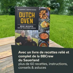 Ein Rezeptbuch mit dem Titel "Dutch Oven" steht auf einem Tisch. Im Hintergrund ist eine grüne Wiese sichtbar.