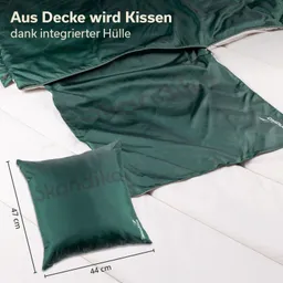 Grüne Decke und Kissen auf einer hellen Oberfläche. Kissen misst 44 cm x 47 cm. Auf der Decke ist der Schriftzug „Skandika“.