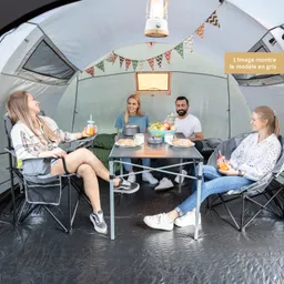 Vier Personen sitzen in einem Zelt um einen Tisch. Auf dem Tisch stehen Lebensmittel und Getränke. Im Hintergrund sieht man eine Girlande.