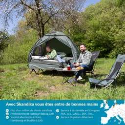 Zelt im Freien mit zwei Personen, eine lesend im Zelt, die andere sitzt daneben auf einem Campingstuhl. Grüne Umgebung.