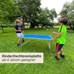 Zwei Personen stehen an einer blauen Kindertischtennisplatte im Freien. Bäume und ein Zaun sind im Hintergrund sichtbar.
