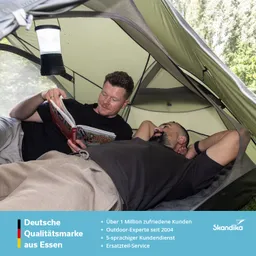 Zwei Personen liegen in einem Zelt. Eine Person liest ein Buch, während die andere entspannt schaut. Eine Lampe hängt an der Zeltwand.
