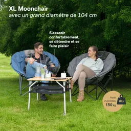 Zwei Personen sitzen entspannt in großen Moonchairs auf einer Wiese. Zwischen ihnen steht ein klappbarer Tisch mit Getränken.