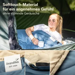 Eine Person liegt in einem Zelt und hält eine Tasse, umgeben von einem blauen Schlafsack. Der Stoff ist sichtbar weich.