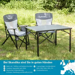 Zwei faltbare Campingstühle und ein Tisch stehen auf einer grünen Wiese. Stühle sind grau und Schwarz.