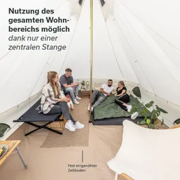 Zeltinnenraum mit einer zentralen Stange. Vier Personen sitzen und stehen auf verschiedenen Schlafgelegenheiten. Möbel und Pflanzen sind sichtbar.