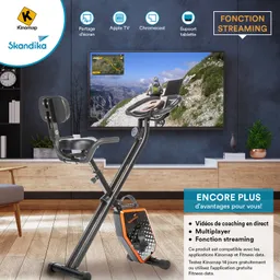 Faltbares Fitnessbike in einem modernen Raum mit Holzfußboden. Im Hintergrund ein Fernseher, der eine Fahrradroute zeigt.