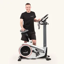 Ein Heimfahrrad mit einem Benutzer, der ohne Helm und in Sportkleidung daran steht und lächelt. Das Fahrrad hat ein modernes Design und trägt das Logo "Skandika".