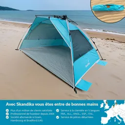 Ein blaues Strandzelt steht auf sandigem Boden, im Hintergrund ist das Meer zu sehen. Ein kleiner Zeltaufbau liegt oben rechts.