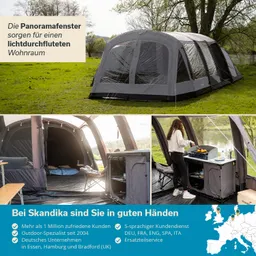 Zelt mit großen Fenstern auf einer Wiese, daneben Küchenecke und Person beim Kochen. Im Hintergrund ein Baum und Wasser.