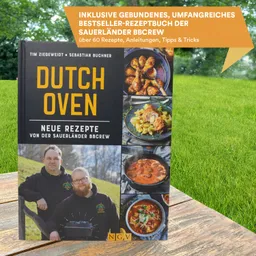 Bilderbuch mit dem Titel "Dutch Oven" auf einer Holzoberfläche, umgeben von grünem Gras. Das Cover zeigt verschiedene Gerichte und zwei Personen.