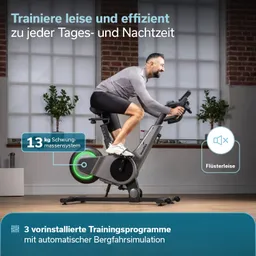 Mann auf einem Trainingsfahrrad in einem hellen Raum mit großen Fenstern und Pflanzen im Hintergrund.