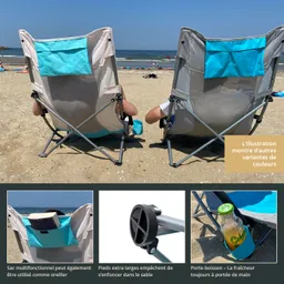 Zwei klappbare Stühle stehen am Strand, Blick auf das Wasser. Auf einem Stuhl sind Füße sichtbar. Es gibt eine Tasche und einen Getränkehalter.