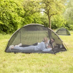 Zwei Personen liegen in einem Zelt auf der Wiese und lesen. Im Hintergrund sind weitere Zelte und Bäume sichtbar.