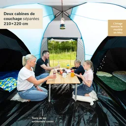 Familie sitzt an einem Tisch im Inneren eines Zeltes. Zwei Kinder und zwei Erwachsene genießen Snacks und Getränke.
