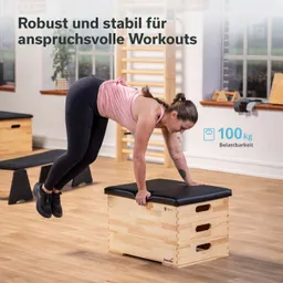 Eine Person in sportlicher Kleidung führt eine Übung auf einem stabilen Holzgerät mit schwarzer Polsterung aus. Im Hintergrund sind weitere Fitnessgeräte sichtbar.
