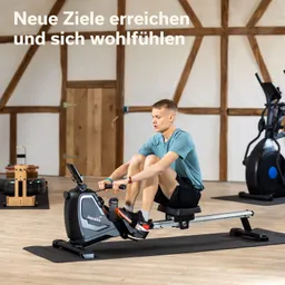 Person sitzt auf einem Rudergerät in einem Raum mit Holzverkleidung, Übungsgeräte im Hintergrund. Holzfußboden sichtbar.