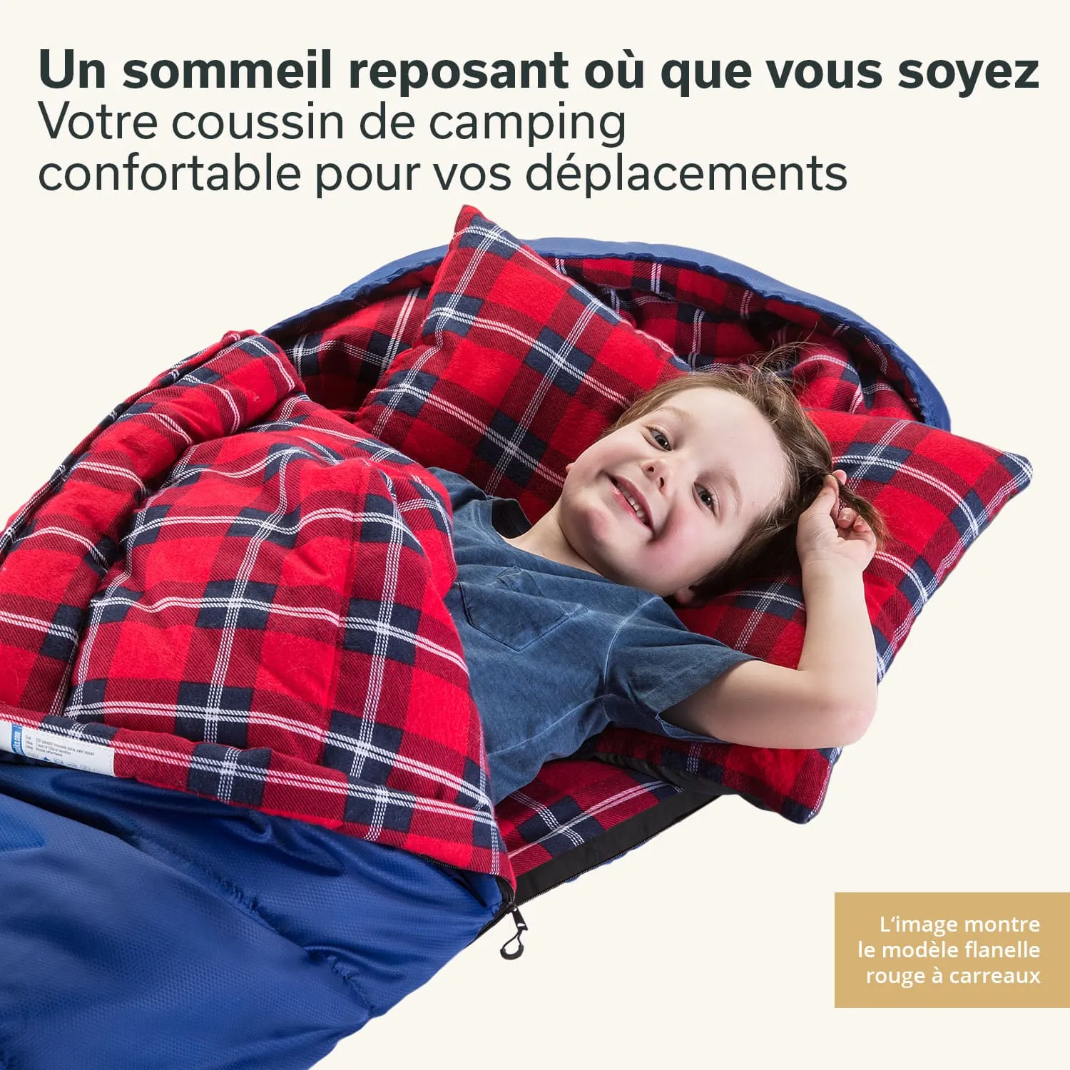 Kind liegt lächelnd in einem schlafsackähnlichen Bett mit kariertem, rot-schwarzem Bezug und blauen Elementen.