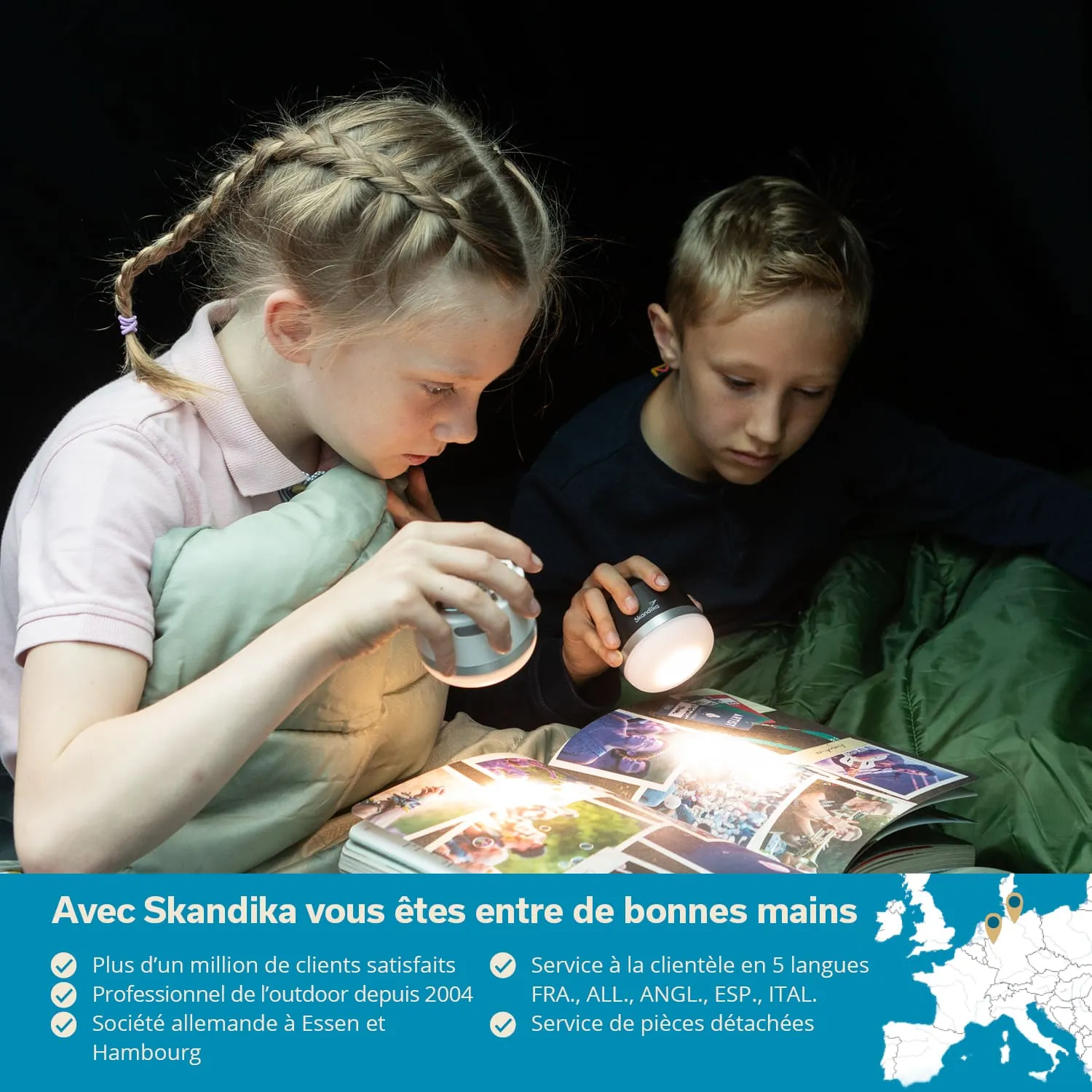 Zwei Kinder lesen mit Taschenlampen in einem Schlafsack. Ein Mädchen mit geflochtenem Haar und ein Junge betrachten ein Bilderbuch.