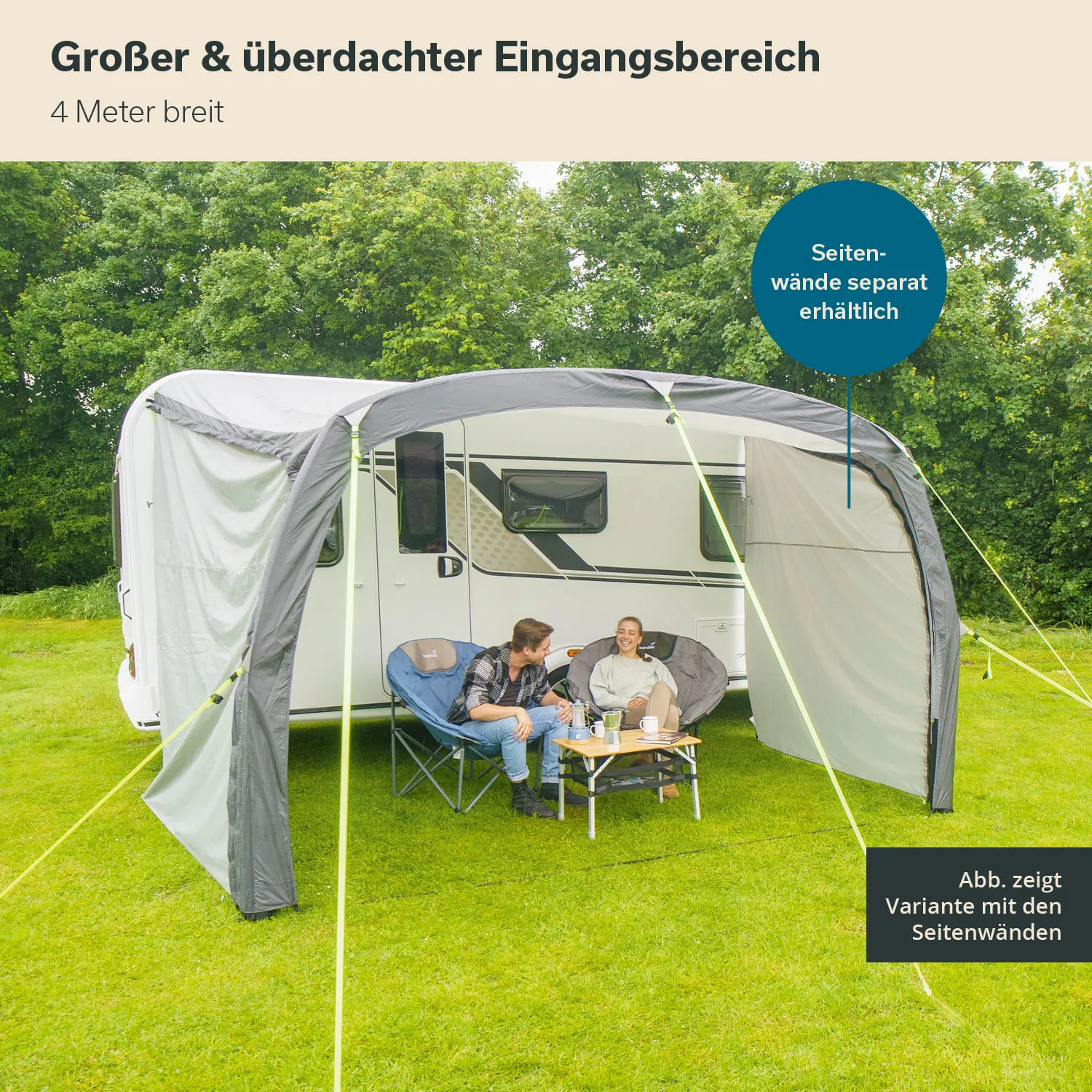 Überdachter Eingangsbereich neben einem Wohnwagen, zwei Personen sitzen auf Faltstühlen, Tee- oder Kaffeetisch mit Getränken.