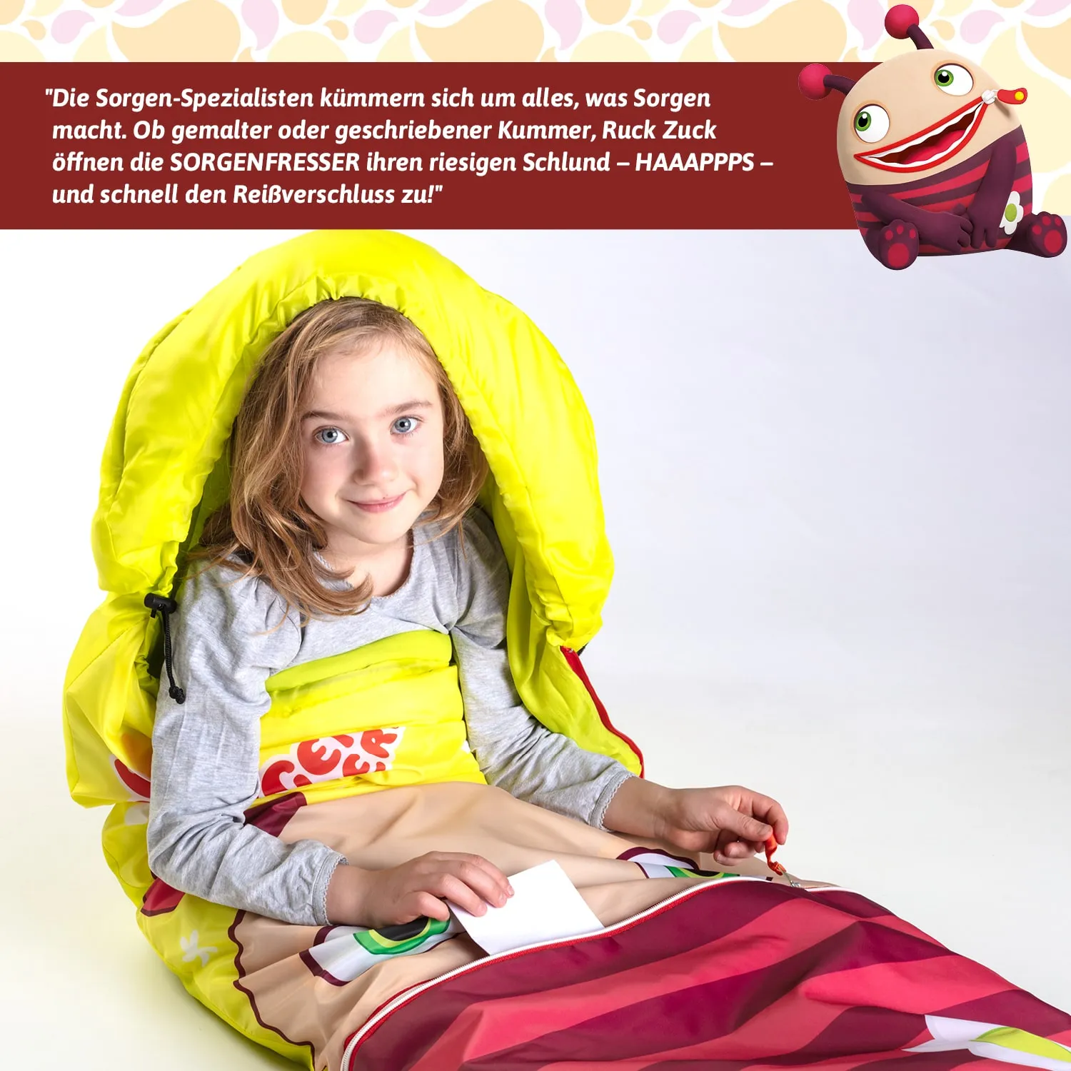 Ein Kind sitzt in einem bunten, gelben Schlafsack. Es hält ein weißes Blatt in der Hand und lächelt. Im Hintergrund ist ein grafisches Element eines cartoonhaften Monsters zu sehen.