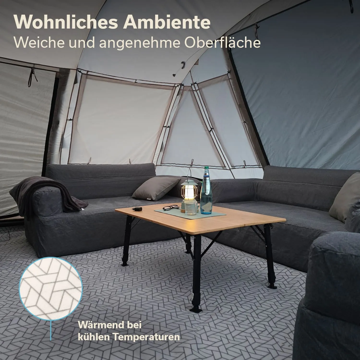 Gemütliche Sitzecke mit grauem Sofa, Tisch aus Holz und Wasserflaschen in einem Zelt mit strukturierter Bodenfläche.