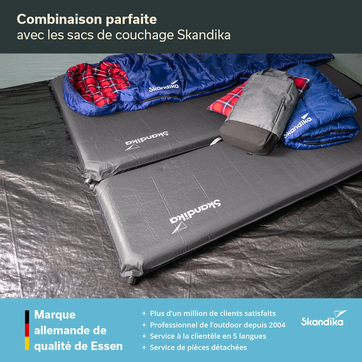 Zwei schwarze Schlafmatten mit dem Logo „Skandika“ liegen nebeneinander. Darauf befinden sich zwei blaue Schlafsäcke und ein Rucksack.