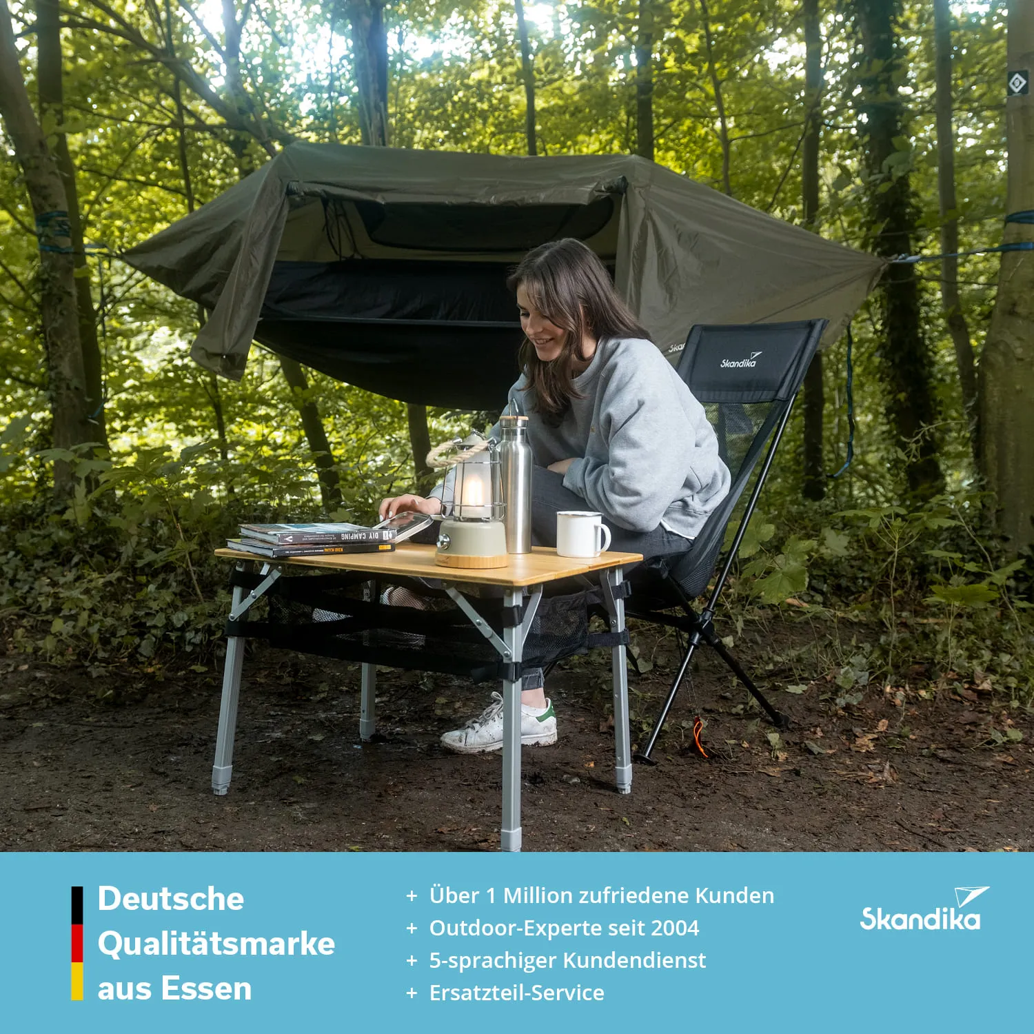 Person sitzt an einem Tisch in einem Wald, mit einem Laptop, einer Lampe und einer Tasse. Im Hintergrund steht ein Zelt.