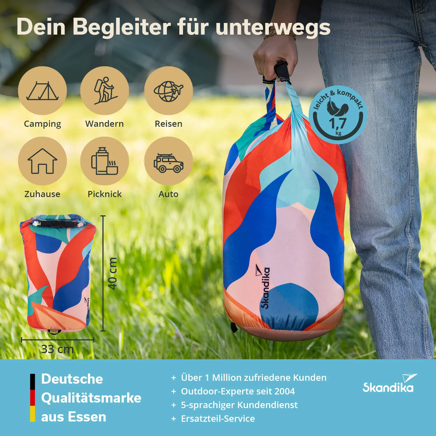 Bunte, zusammengerollte Tragetasche mit Grafikdesign, gehalten von einer Person in Jeans. Hintergrund mit Gras und Zelt.