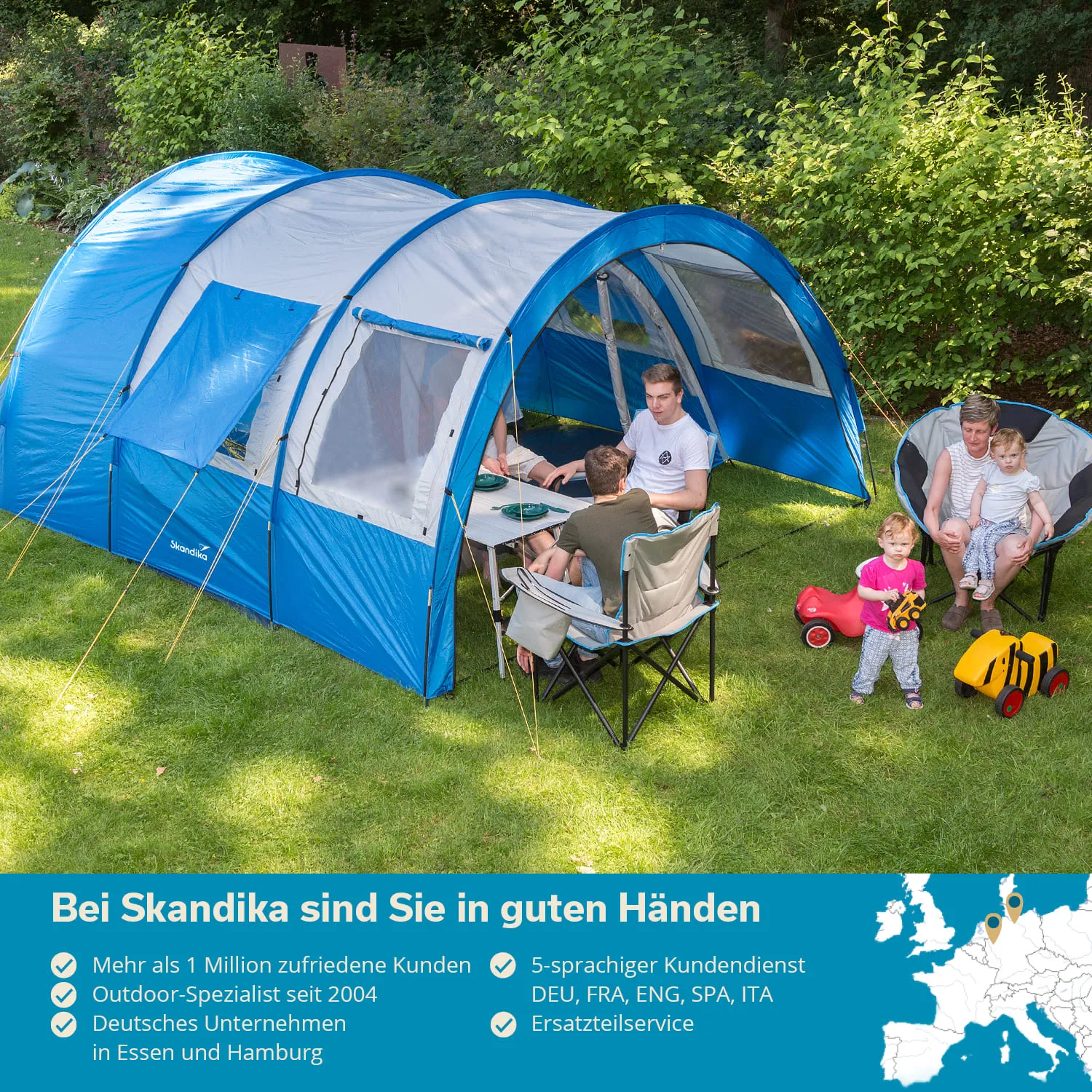 Zelt mit blauer Plane auf einer Wiese. Zwei Erwachsene und ein Kind am Tisch, zwei Kinder spielen. Grüne Bäume im Hintergrund.