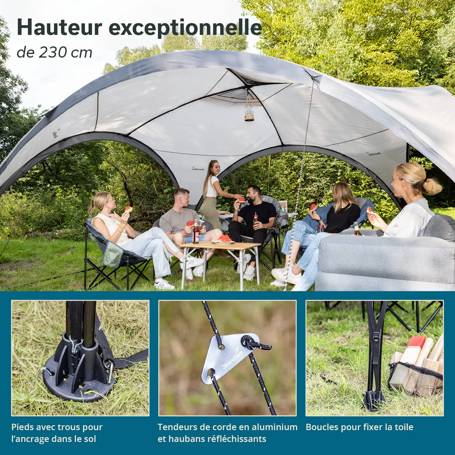 Zelt mit großer Höhe und mehreren Personen, die auf Campingstühlen sitzen und essen. Grüne Wiese im Hintergrund.