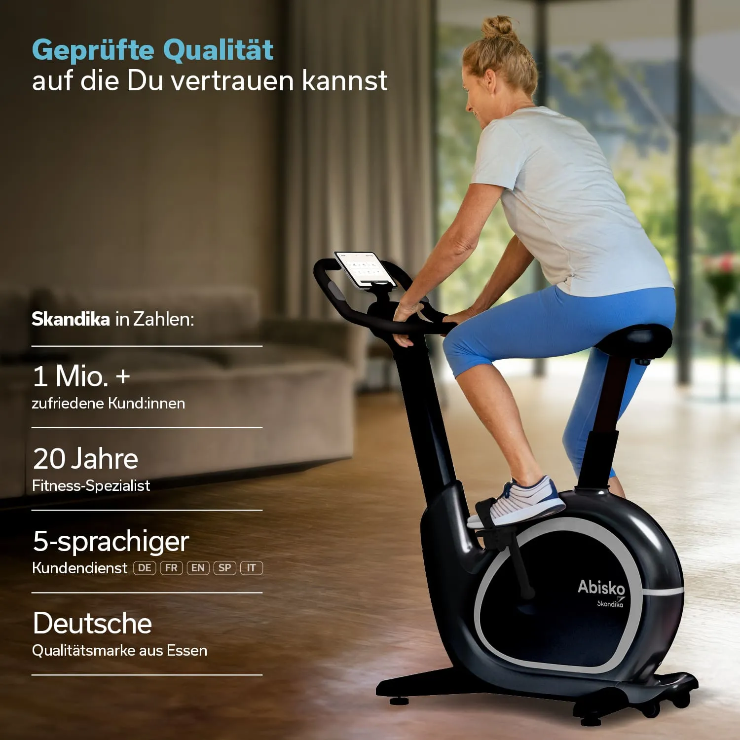 Ein Mann sitzt auf einem schwarzen Heimtrainer und betrachtet einen Bildschirm. Der Raum ist hell und modern eingerichtet.