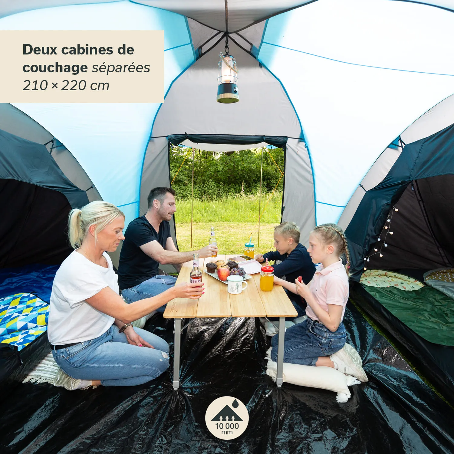 Familie sitzt in einem Zelt an einem Tisch. Die Personen haben Getränke und Snacks vor sich. Zwei Kabinen sind im Hintergrund sichtbar.