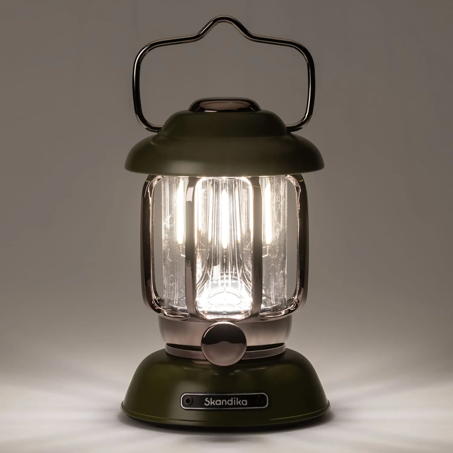 Grüne Laterne mit transparentem Glas, versilbertem Griff und einer Bedientaste, leuchtet sanft im Vordergrund.