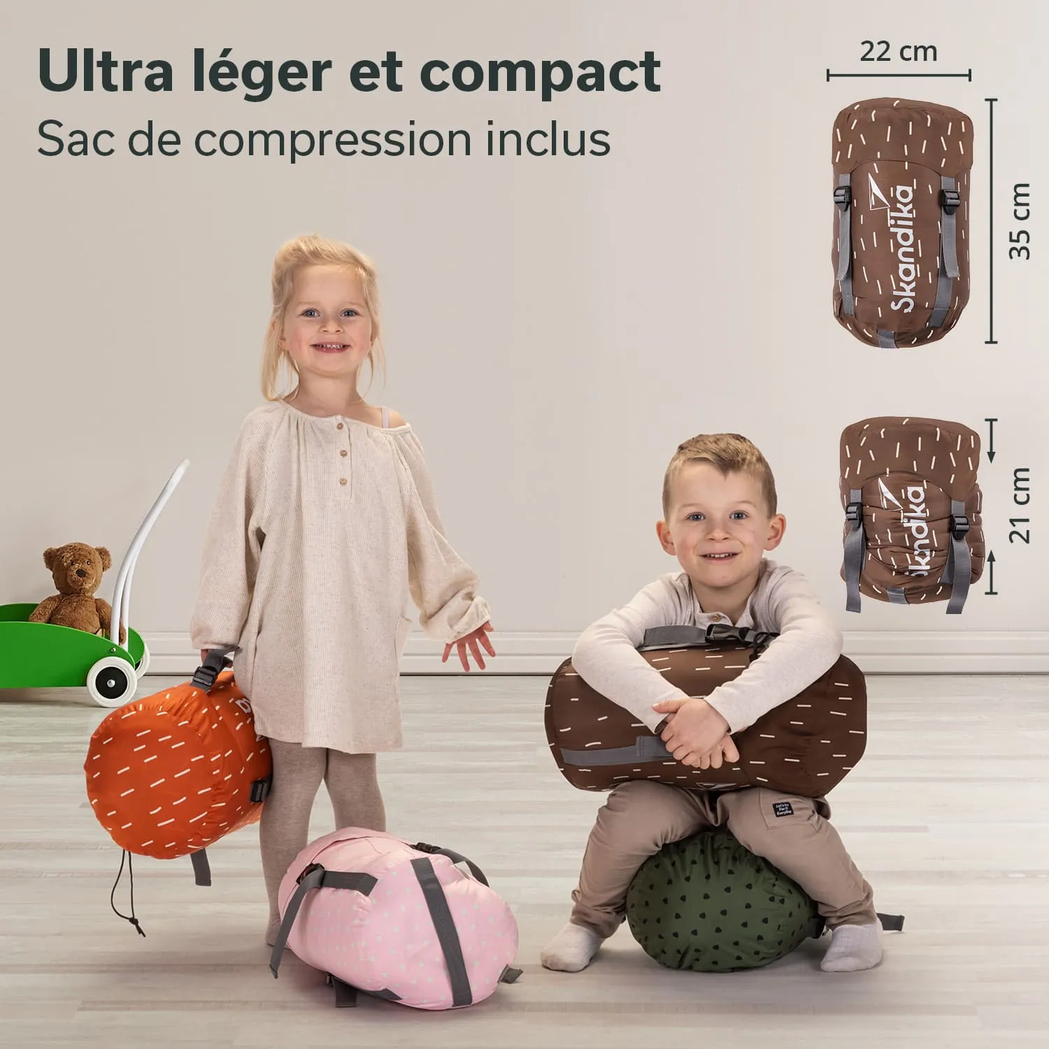 Zwei Kinder stehen mit farbigen, gepolsterten Taschen. Die Mädchen trägt ein helles Oberteil und steht neben einer orangenen Tasche, während das Mädchen sitzt, eine graue Tasche umarmend.