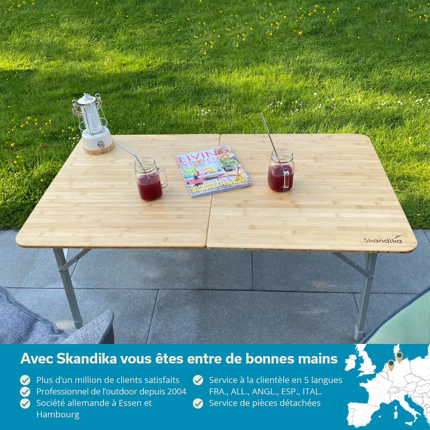 Tisch aus Holz mit zwei Gläsern, einer Zeitschrift und einer Laterne auf grünem Rasen im Hintergrund.