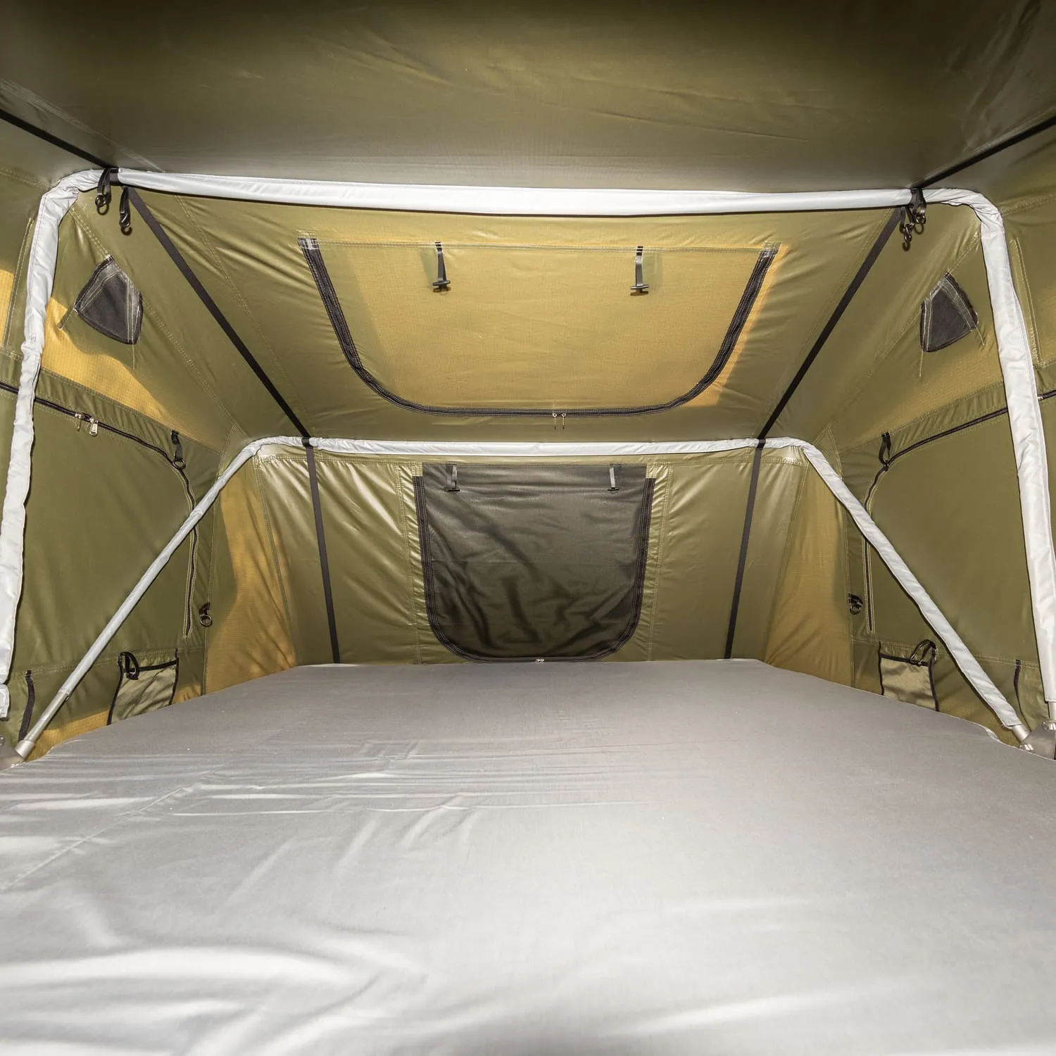 Innansicht eines Zeltzimmers mit einem grauen Bett und olivgrünen Wänden. Fenster und Belüftungsöffnungen sind sichtbar.